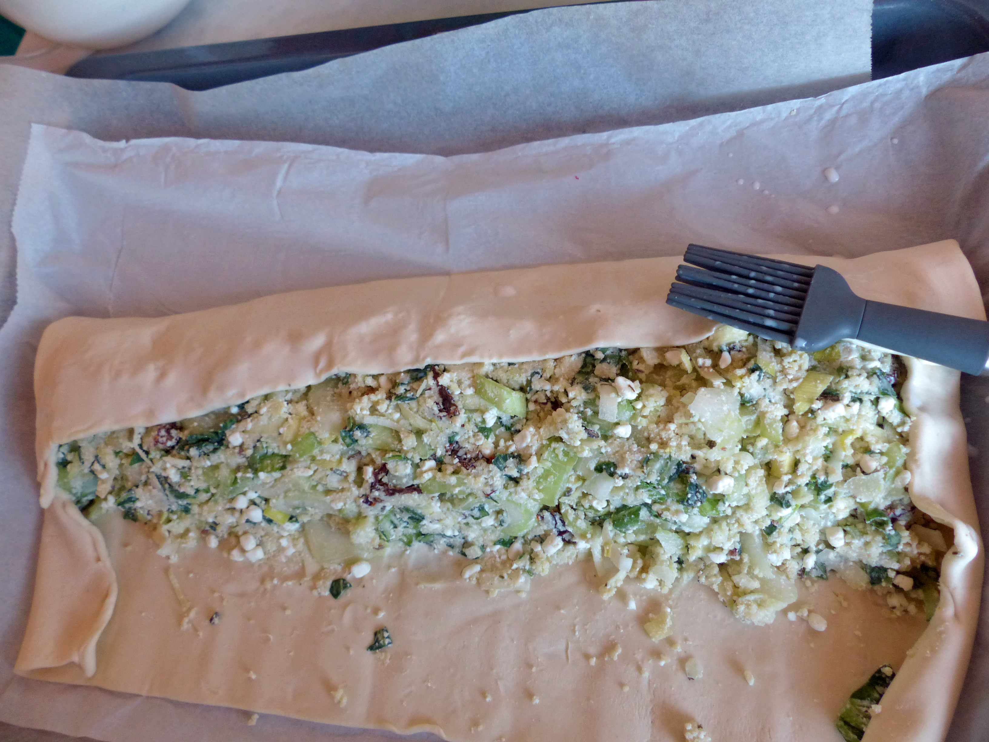 <p>Eine Strudel-Längsseite zur Mitte des Strudels ziehen. Das Backpapier hilft dabei.</p>