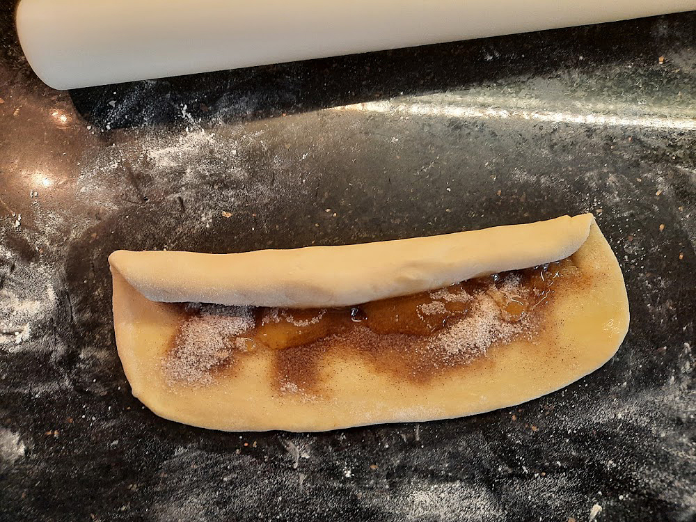 <p>Die belegte Teigplatte wird von einer Längsseite her straff aufgerollt.</p>