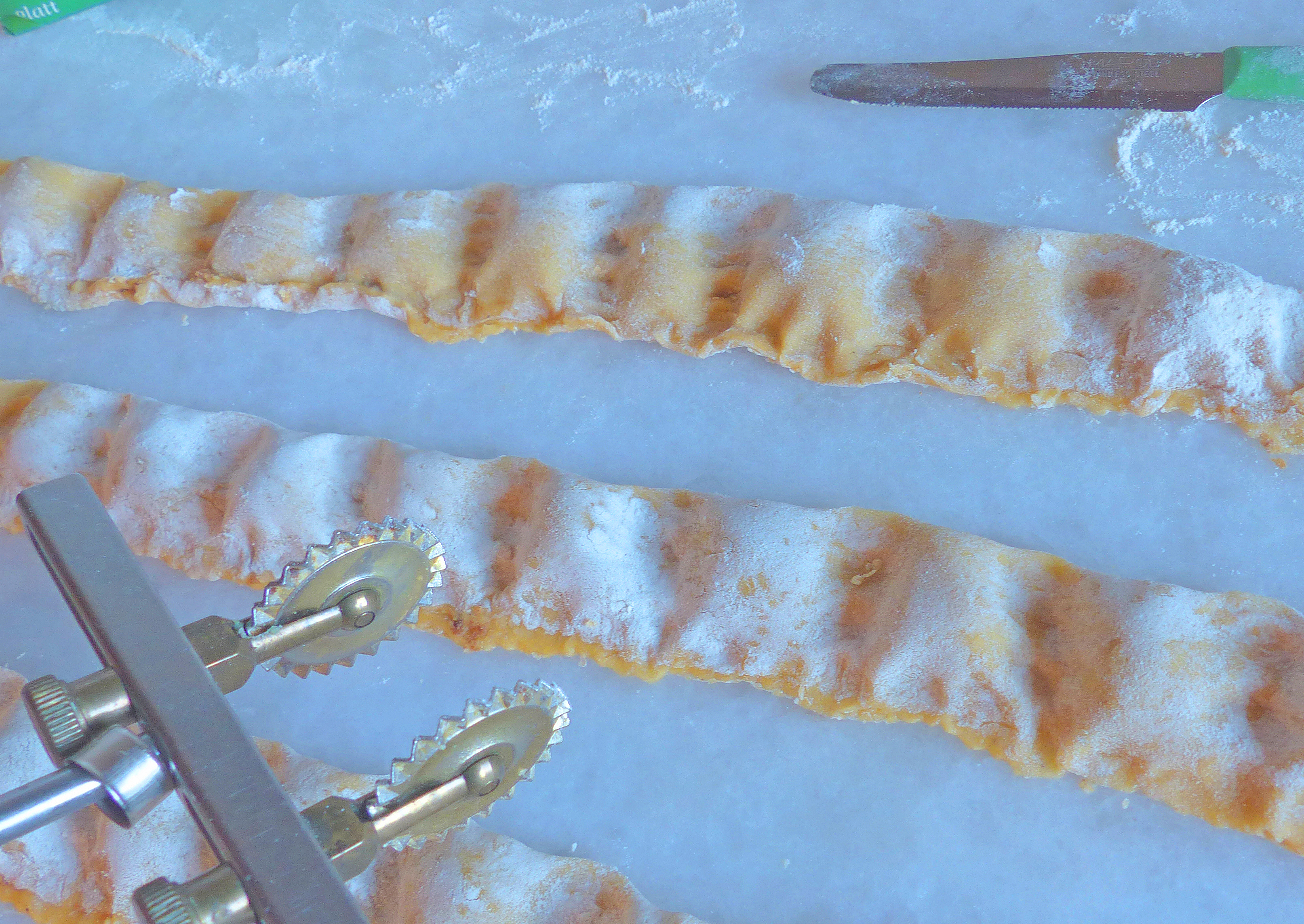 <p>Mit einem Teigrädchen oder Messer wird der gefüllte Teigstreifen in viereckige Ravioli geschnitten.</p>
