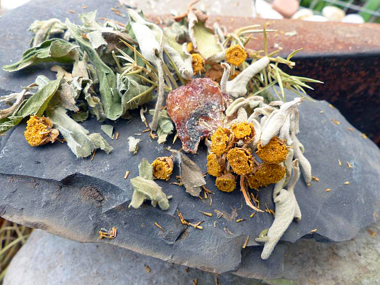 <p>Räucherwerk verglimmt duftend auf einem flachen, heißen Stein am Rande eines Feuers</p>