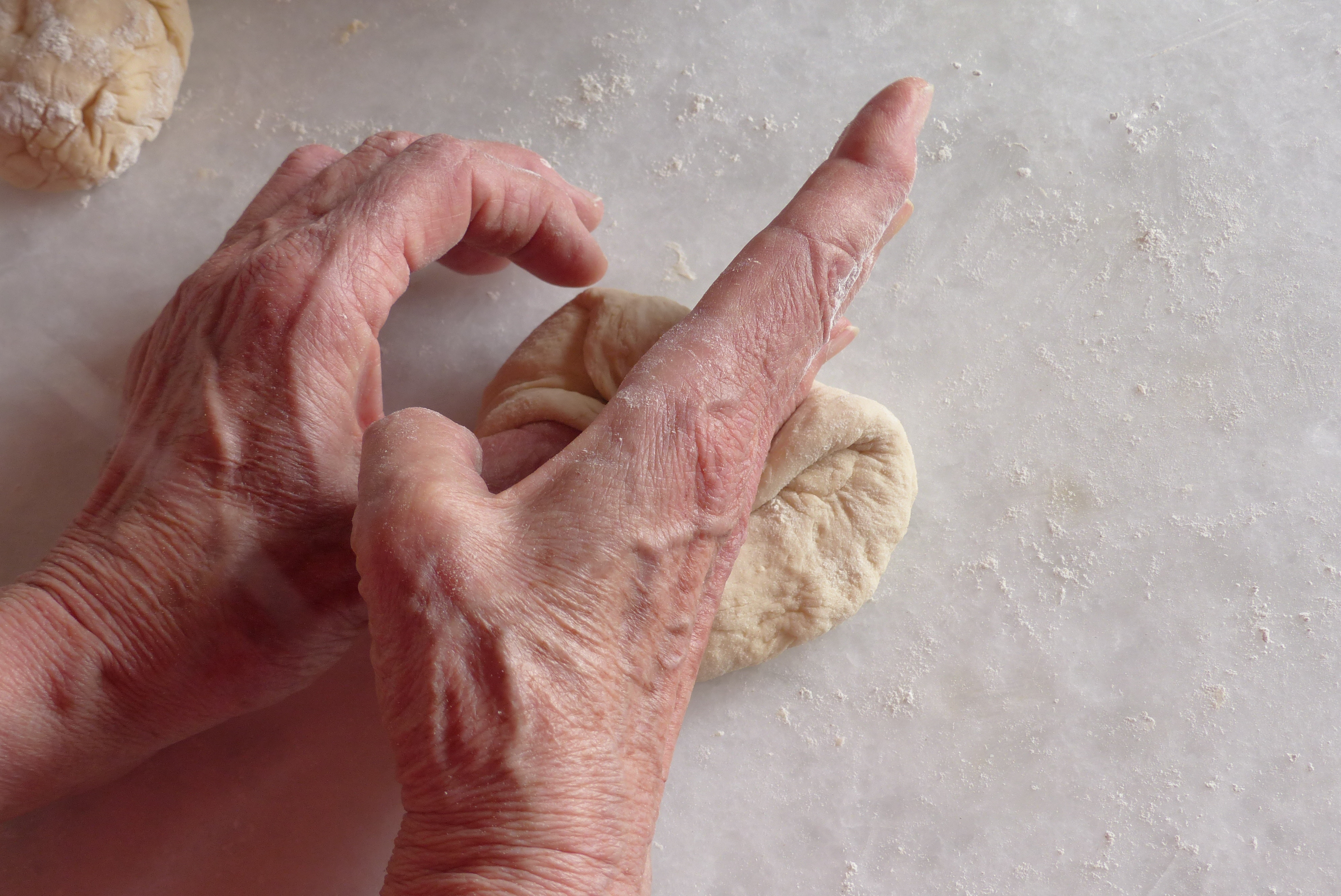 <p>Mit der Handkante drückt („schlägt“) man den rechten Rand des Teiglappens auf den Boden des Fladens.</p>