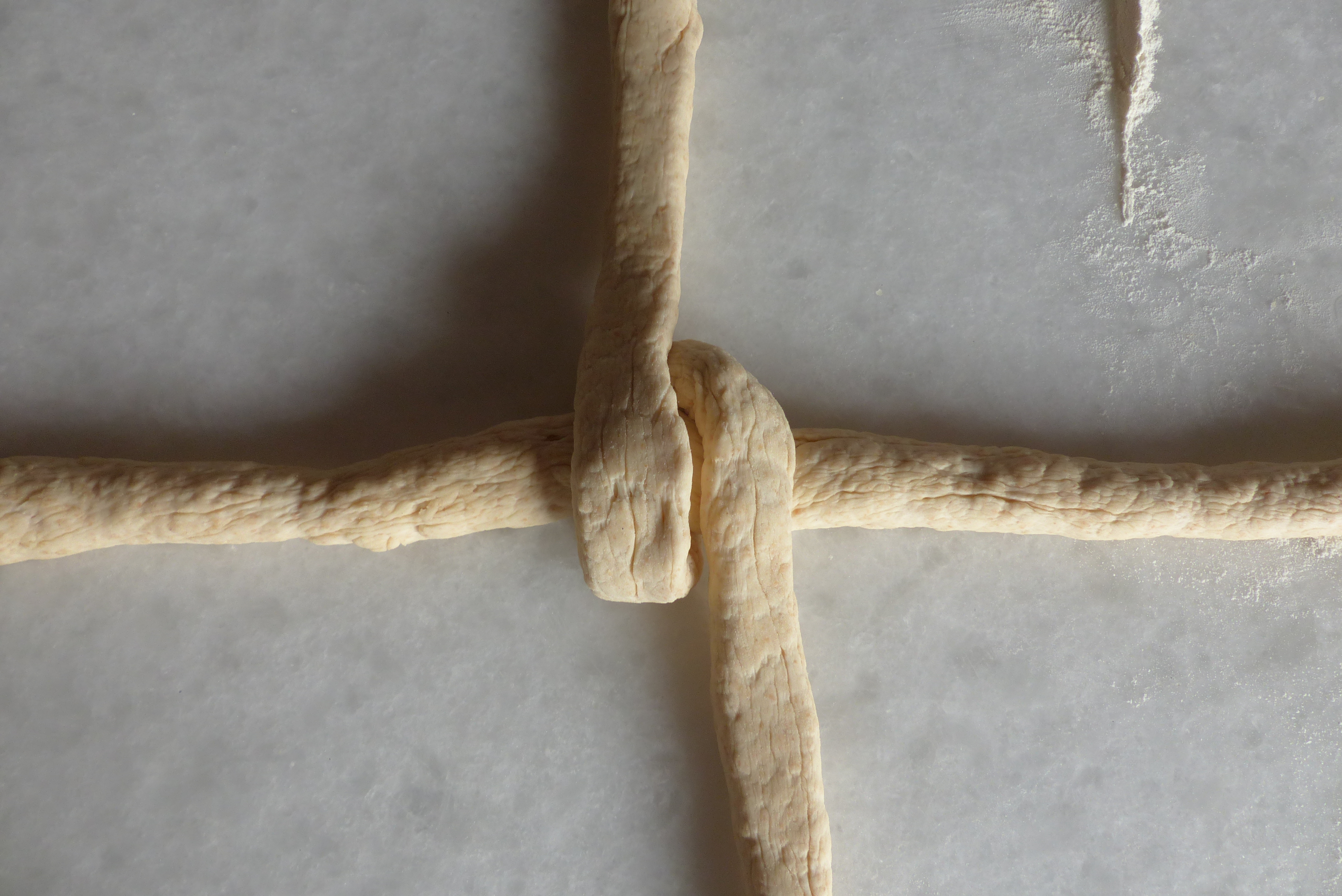 <p>Danach zieht man die untere parallel <strong>links des Kreuzknotens</strong> vorbei nach oben, wo man sie ablegt.</p>