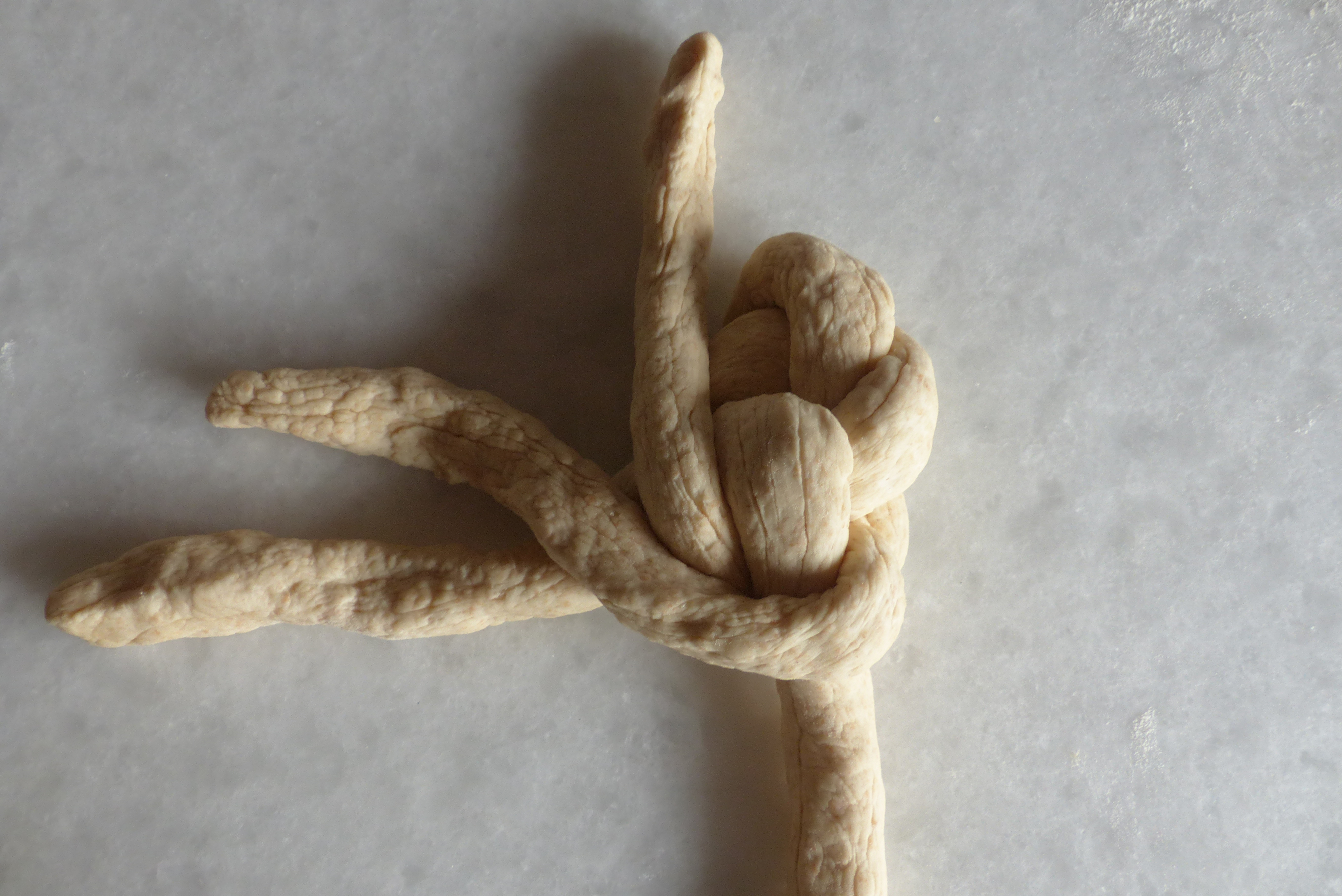 <p>Jetzt zieht man das rechte Strangende <strong>unterhalb</strong> des Mittelpunkts vorbei nach links und legt es parallel <em><strong>oberhalb</strong></em> der liegenden waagrechten Stranghälfte ab. </p>