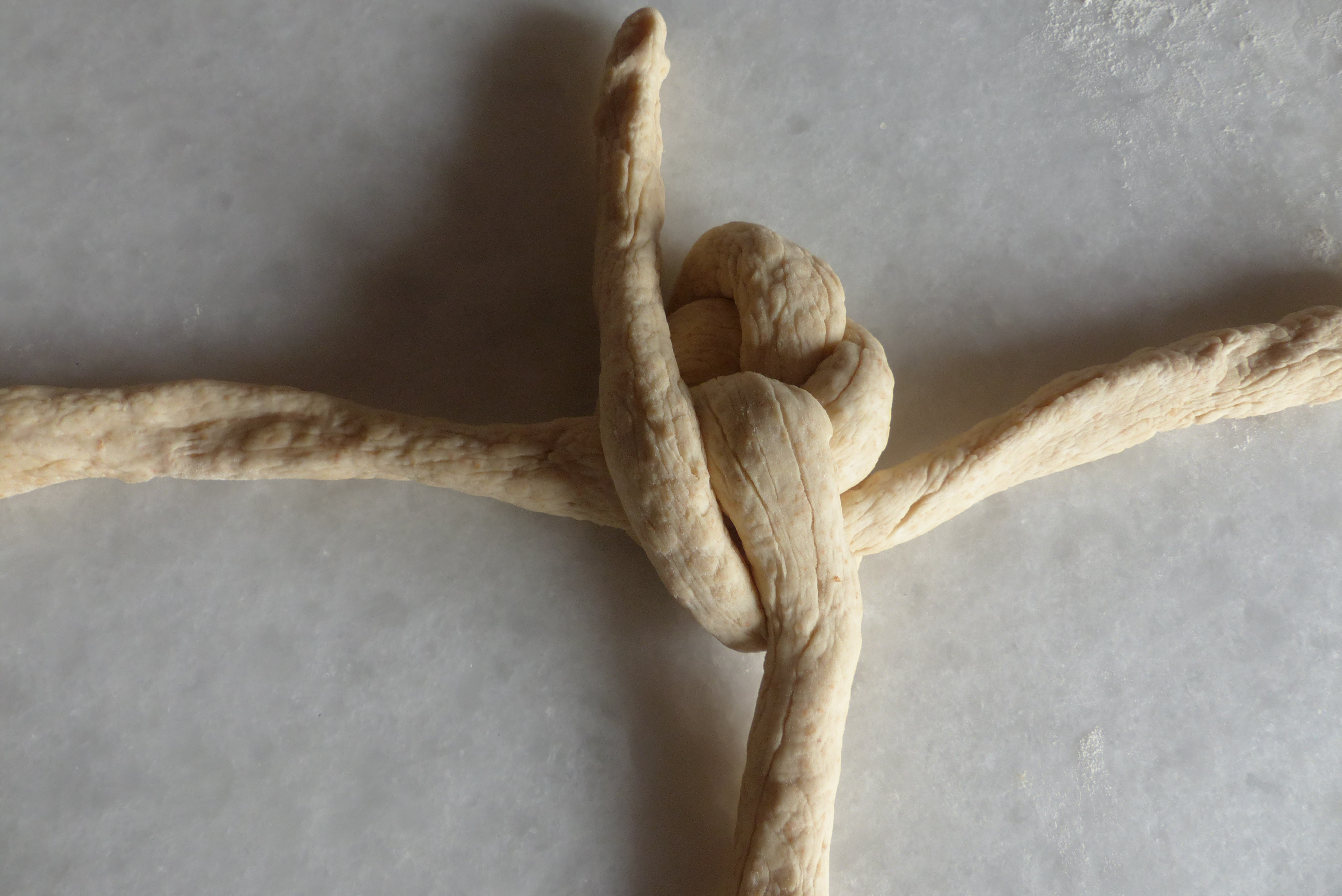 <p>Danach zieht man die untere parallel <strong>links des Kreuzknotens</strong> vorbei nach oben, wo man sie ablegt. </p>