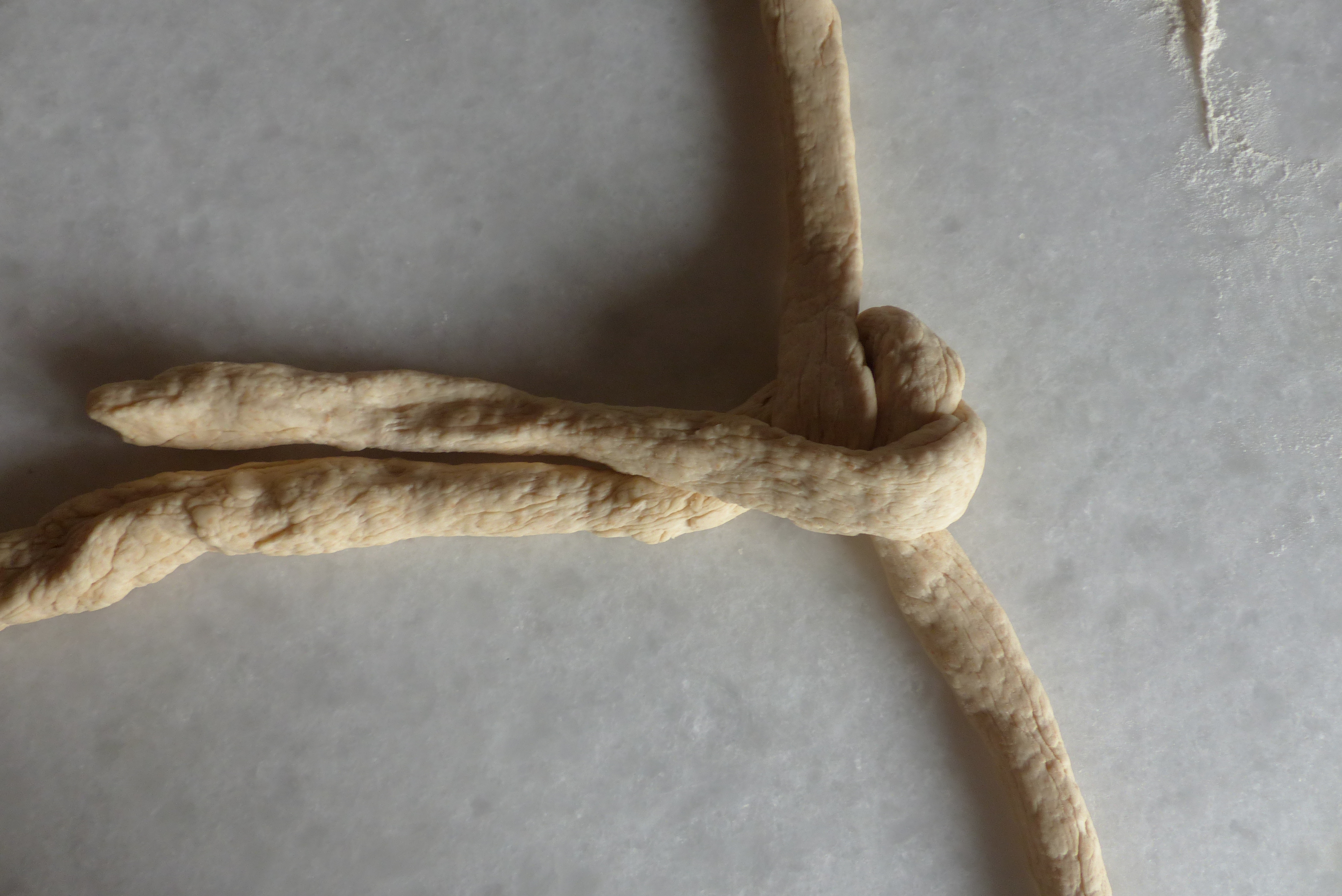 <p> Jetzt zieht man das rechte Strangende <strong>unterhalb</strong> des Mittelpunkts vorbei nach links und legt es parallel <em><strong>oberhalb</strong></em> der liegenden waagrechten Stranghälfte ab. </p>