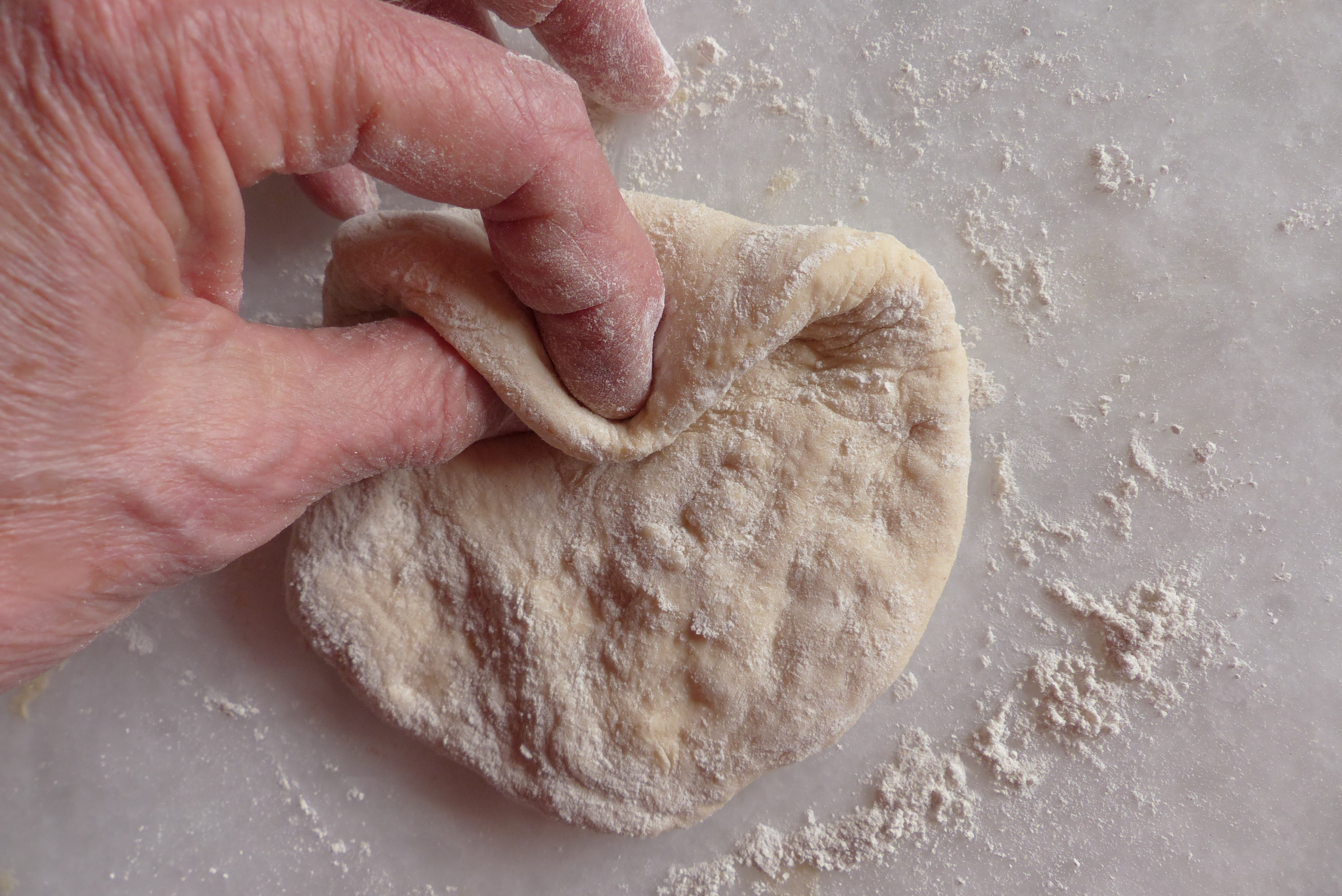 <p>Ein Stück Teigrand wird zum Daumen gezogen. Es bildet sich automatisch ein dreieckiger Teiglappen.</p>
