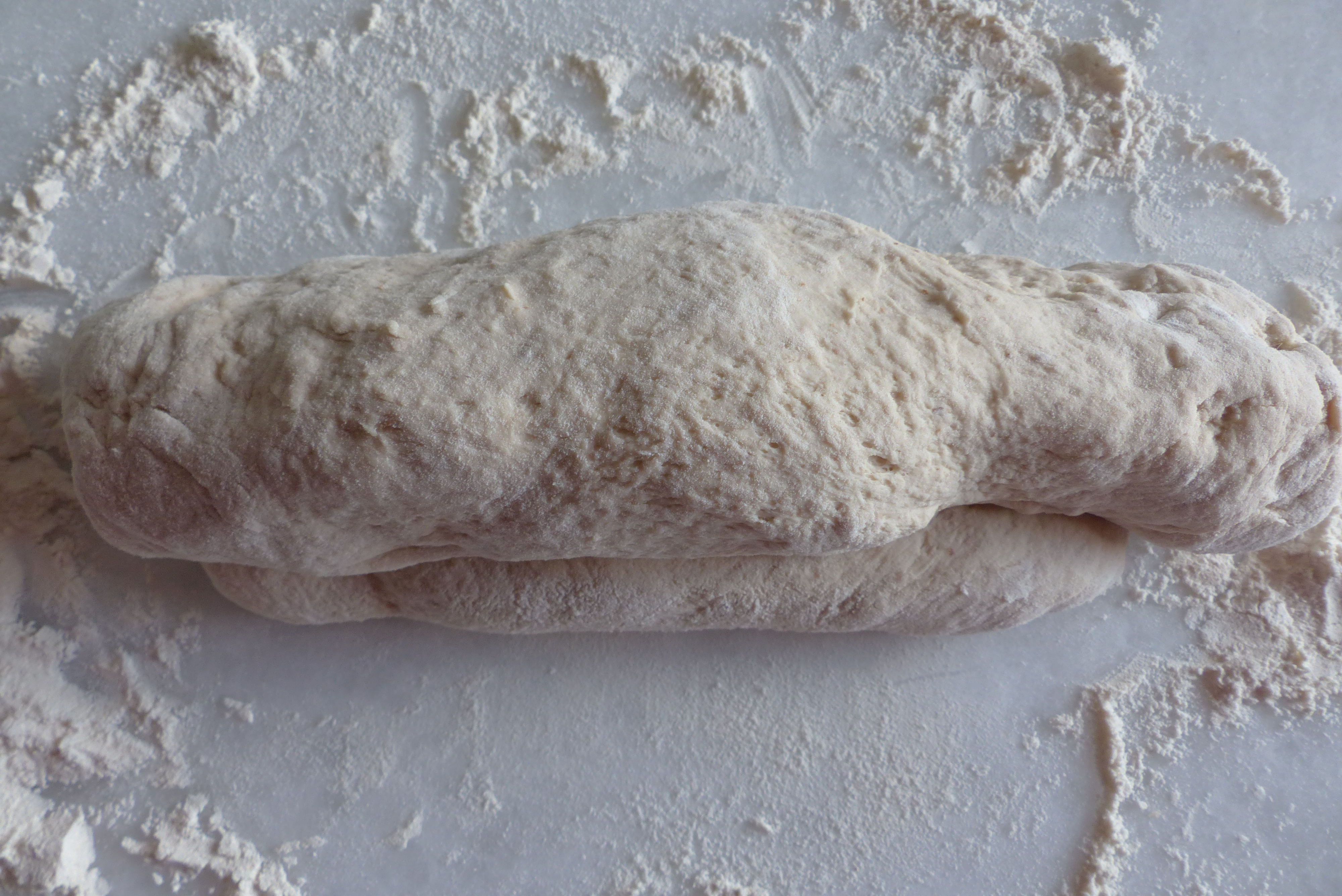 <p>Die beiden <strong>Längsseiten aufeinander </strong>legen und durch Drücken<em> </em>verschließen (= "Teigschluss")<em>. </em>Danach den Teigling so rollen, dass er mit seinem <strong>Teigschluss nach unten</strong> zu liegen kommt. </p>