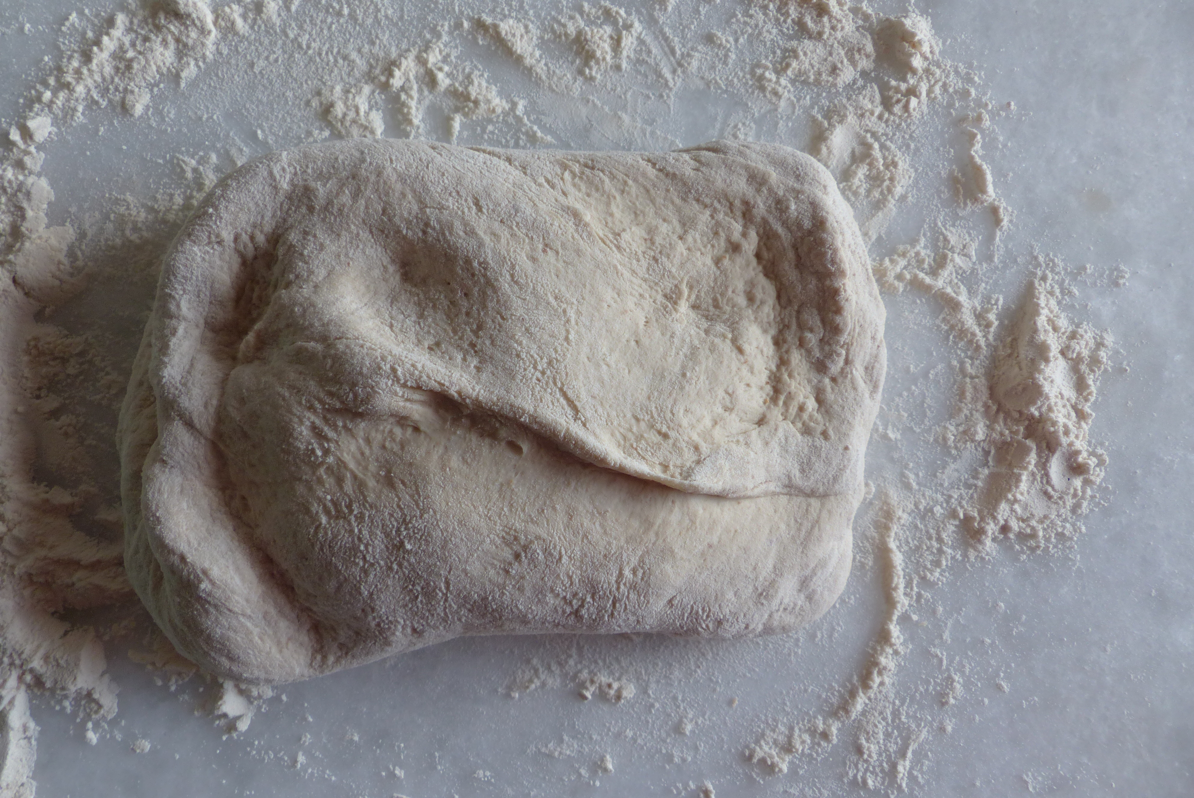 <p>Das <strong>quadratische Teigpaket</strong> mit seinem <strong>Teigschluss nach oben</strong> liegend mit Gefühl <strong>dehnen und flachdrücken, </strong>beinahe so lang wie die gewünschte Brotlänge.</p>